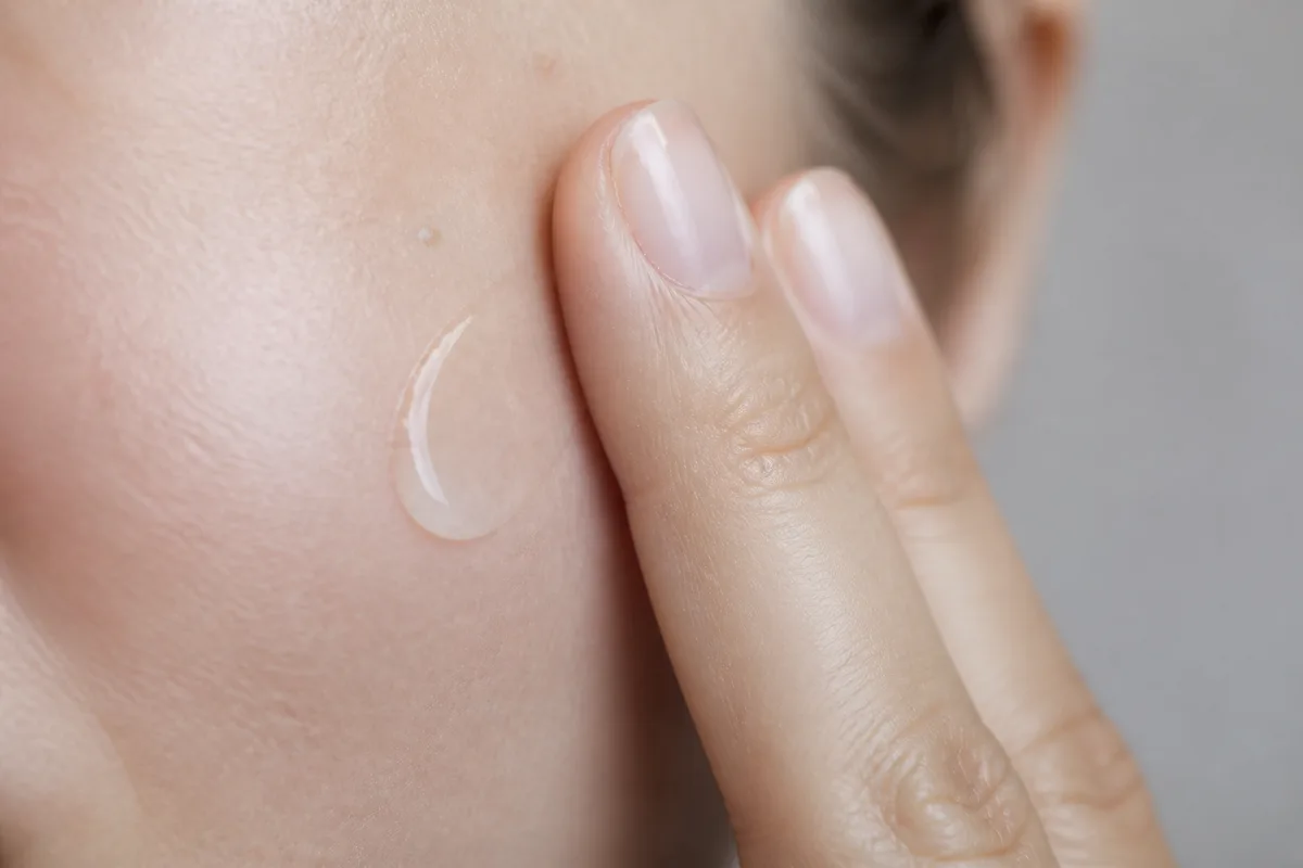 Main appliquant une texture fluide sur une joue, gros plan lumière naturelle